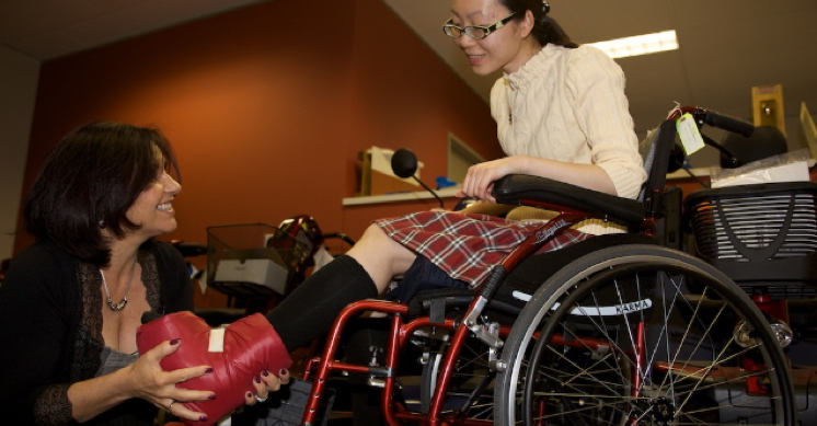 An ILC occupational therapist helping young girl fit leg cast in wheelchair.